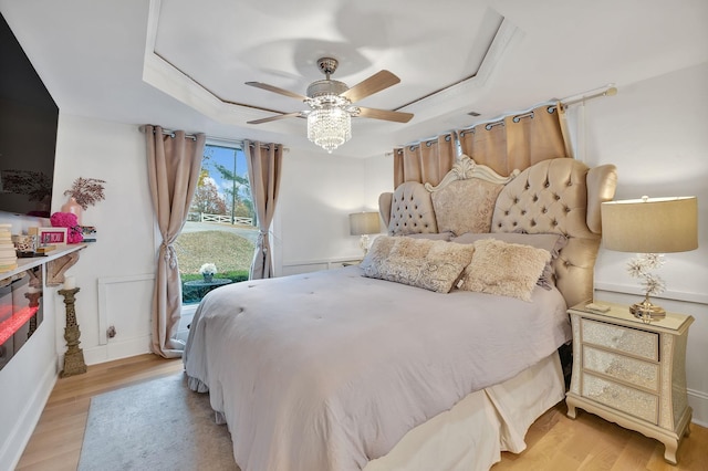 bedroom featuring light wood-type flooring, a tray ceiling, and ceiling fan