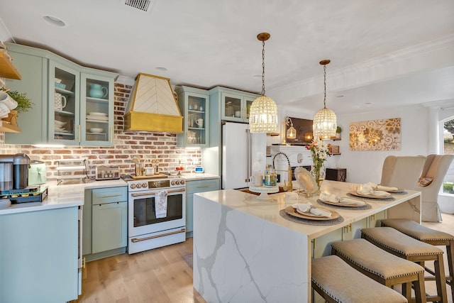 kitchen with premium range hood, white appliances, pendant lighting, light hardwood / wood-style floors, and an island with sink