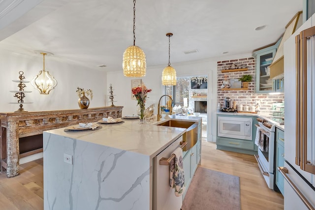 kitchen with light stone countertops, pendant lighting, white appliances, light hardwood / wood-style floors, and a center island with sink