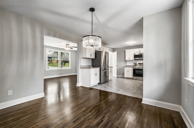 kitchen with dark wood-type flooring, pendant lighting, white cabinets, ceiling fan with notable chandelier, and appliances with stainless steel finishes