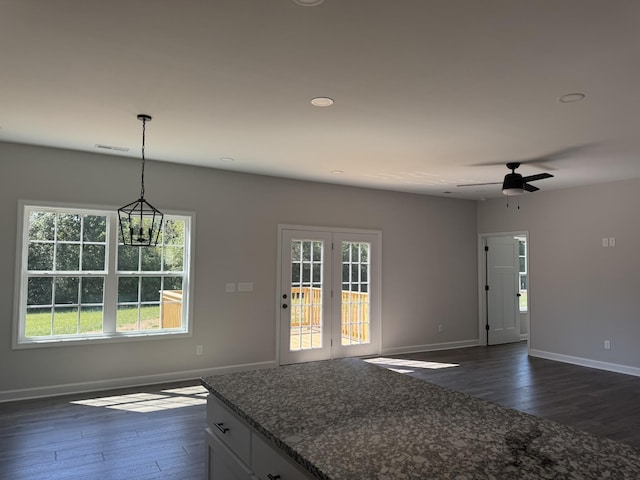 kitchen featuring dark wood-type flooring, hanging light fixtures, dark stone counters, white cabinets, and ceiling fan with notable chandelier