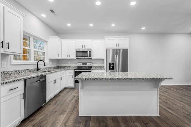 kitchen with visible vents, a kitchen island, white cabinets, stainless steel appliances, and a sink