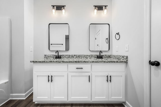 bathroom with double vanity, wood finished floors, baseboards, and a sink