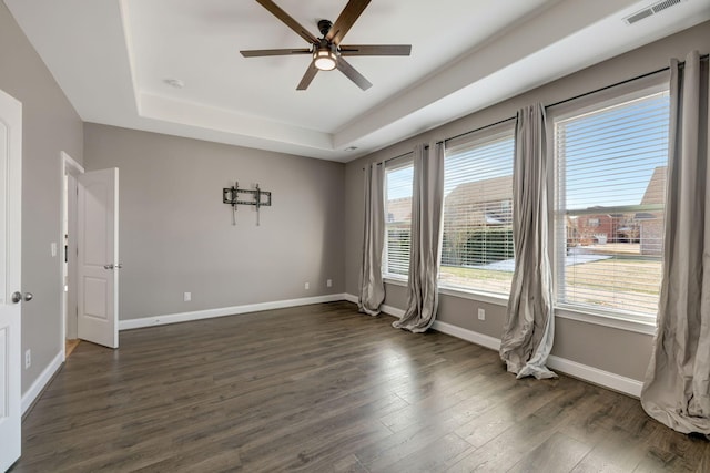 empty room featuring a raised ceiling, ceiling fan, and dark hardwood / wood-style floors