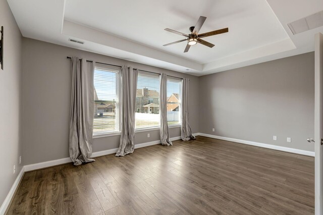 unfurnished room with ceiling fan, dark hardwood / wood-style floors, and a tray ceiling