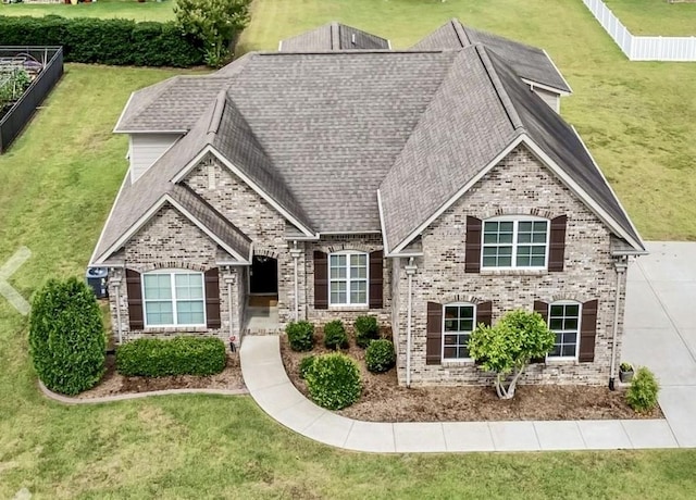 view of front of property featuring a shingled roof, brick siding, fence, and a front lawn