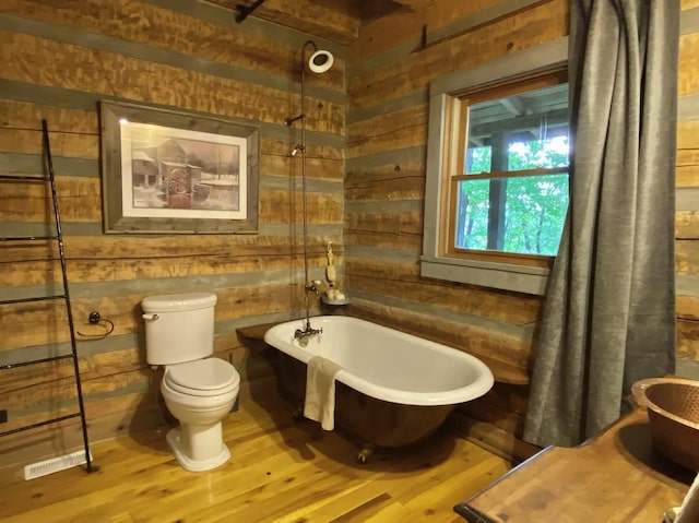 bathroom with a tub, wooden walls, hardwood / wood-style floors, and toilet