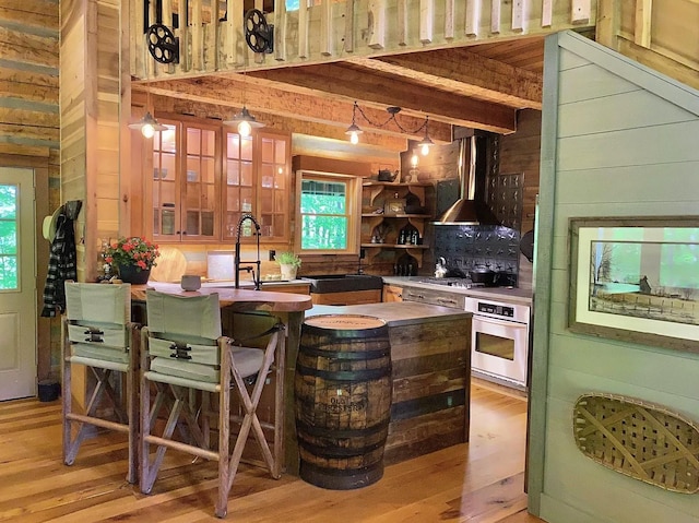 bar featuring stainless steel oven, hanging light fixtures, light hardwood / wood-style flooring, extractor fan, and wooden walls