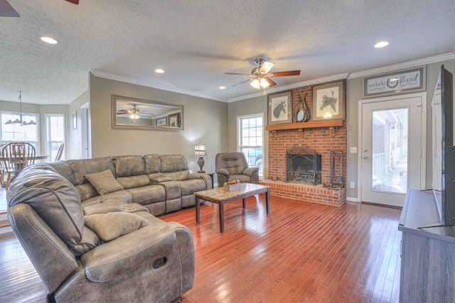 living room featuring hardwood / wood-style floors, ceiling fan with notable chandelier, a fireplace, and a textured ceiling