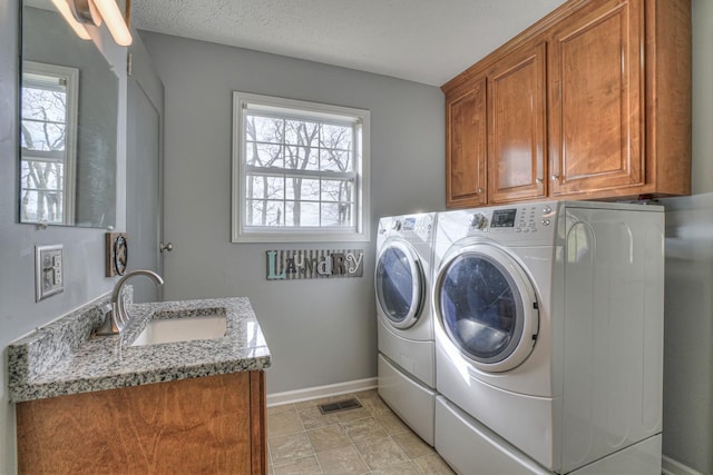 laundry room with a textured ceiling, cabinets, separate washer and dryer, and sink