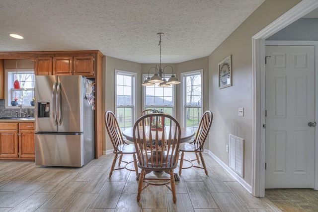 dining room featuring sink, light hardwood / wood-style floors, a textured ceiling, and a notable chandelier