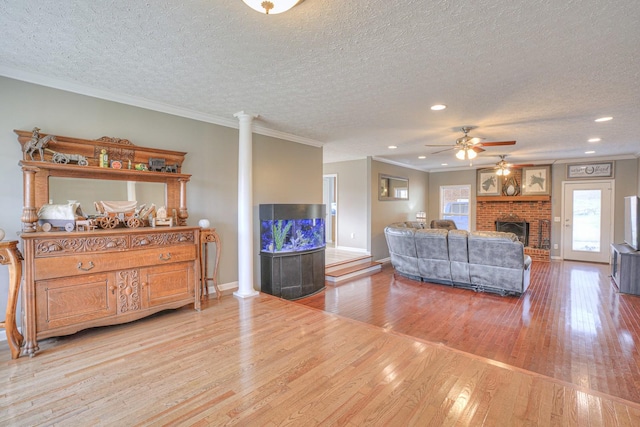 living room with light wood-type flooring, ornate columns, a textured ceiling, crown molding, and a fireplace