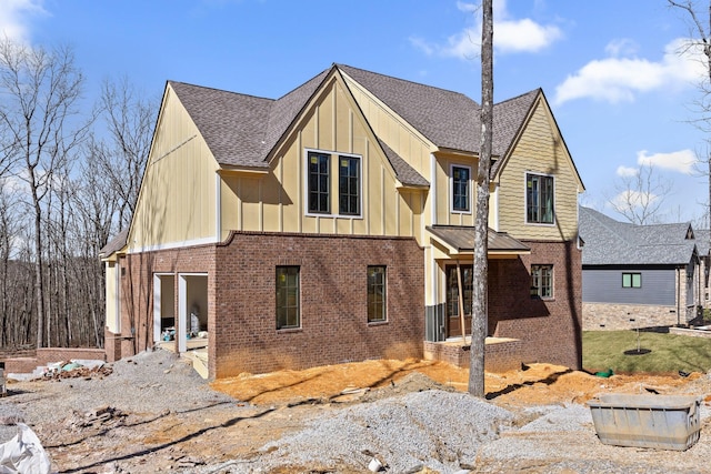 view of front facade with roof with shingles, board and batten siding, and brick siding