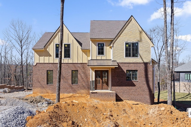 view of front facade featuring a standing seam roof, roof with shingles, brick siding, and board and batten siding