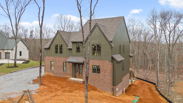 view of front facade with brick siding, board and batten siding, a shingled roof, and gravel driveway