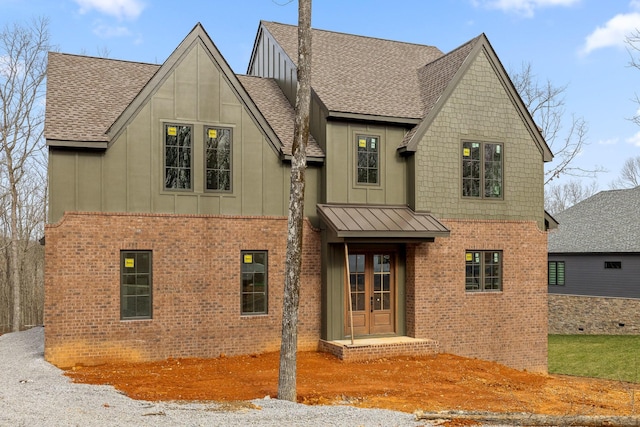 view of front facade with brick siding, french doors, a shingled roof, and board and batten siding