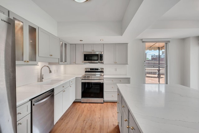 kitchen with light stone countertops, appliances with stainless steel finishes, sink, gray cabinets, and light hardwood / wood-style floors