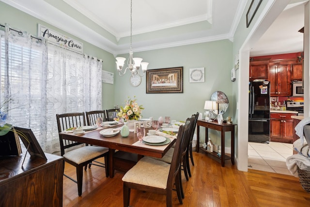 dining room with light wood-style floors, a notable chandelier, a raised ceiling, and crown molding