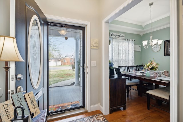 entryway with a tray ceiling, crown molding, an inviting chandelier, wood finished floors, and baseboards