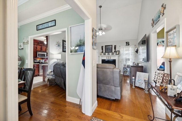 living area with ceiling fan, a fireplace, wood finished floors, vaulted ceiling, and ornamental molding