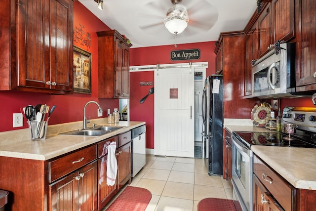 kitchen with light tile patterned floors, a barn door, stainless steel appliances, a sink, and light countertops