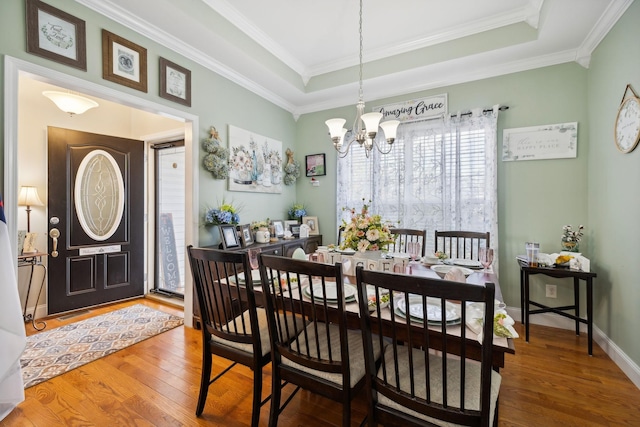 dining room featuring ornamental molding, a raised ceiling, a notable chandelier, and wood finished floors