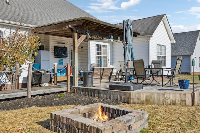 exterior space with a fire pit, a deck, and roof with shingles