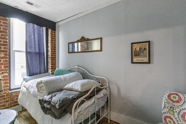 bedroom featuring hardwood / wood-style floors, a textured ceiling, and brick wall