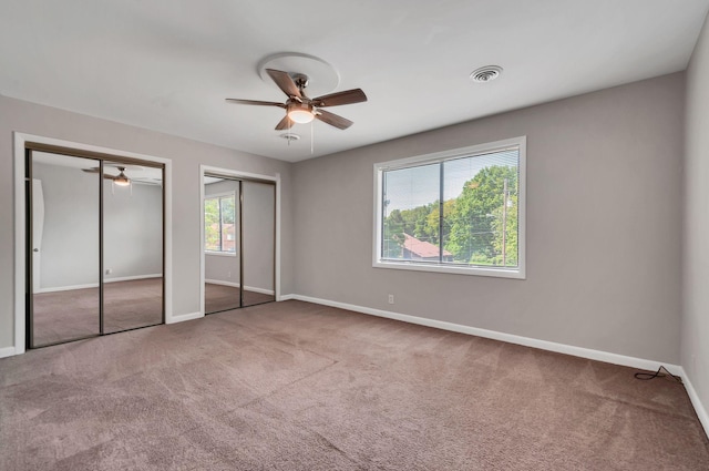 unfurnished bedroom with carpet, ceiling fan, two closets, and multiple windows