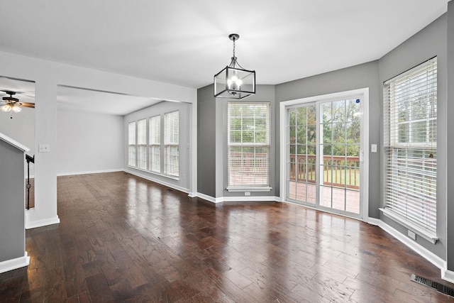 unfurnished dining area with ceiling fan with notable chandelier and dark wood-type flooring