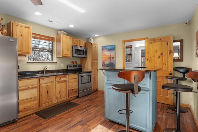 kitchen featuring sink, dark wood-type flooring, stainless steel appliances, a kitchen breakfast bar, and dark stone countertops