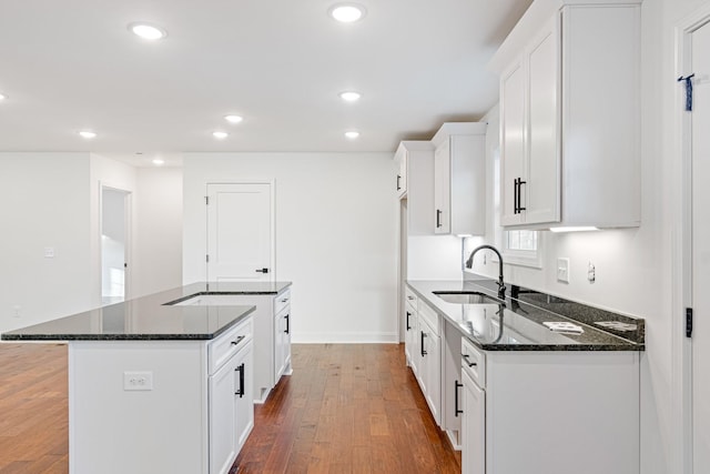 kitchen featuring dark wood-type flooring, dark stone counters, sink, a kitchen island, and white cabinetry