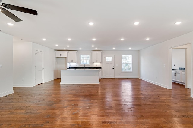 unfurnished living room with ceiling fan, sink, and dark wood-type flooring