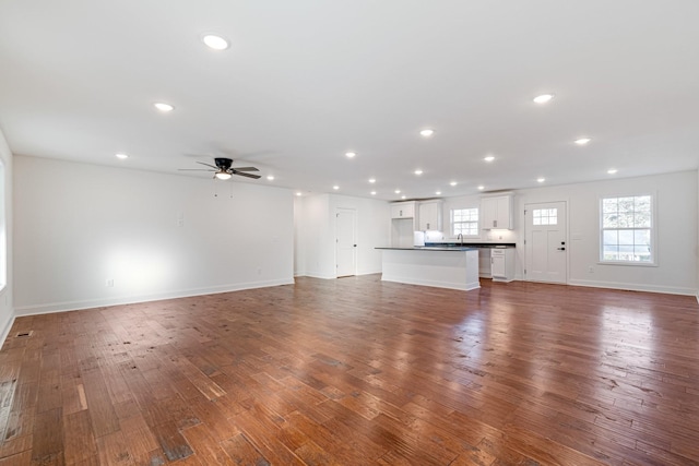 unfurnished living room featuring ceiling fan and dark wood-type flooring