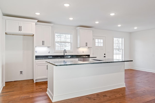 kitchen with white cabinets, a center island, dark stone countertops, and hardwood / wood-style flooring