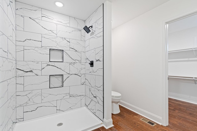 bathroom with toilet, a tile shower, and wood-type flooring