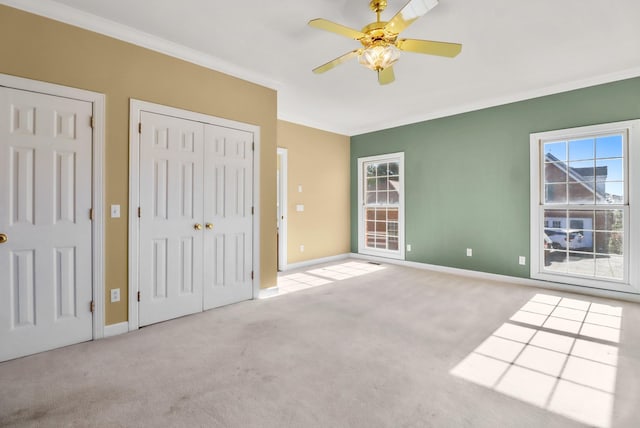 unfurnished bedroom with ceiling fan, crown molding, light carpet, and multiple closets