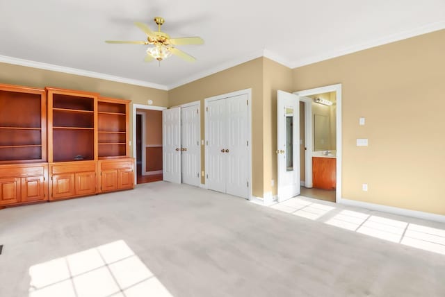 unfurnished bedroom with ensuite bath, ceiling fan, light colored carpet, two closets, and ornamental molding