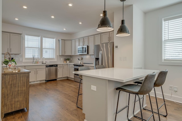 kitchen featuring appliances with stainless steel finishes, backsplash, a kitchen breakfast bar, light hardwood / wood-style floors, and hanging light fixtures