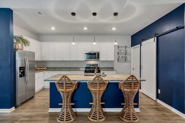 kitchen with pendant lighting, a kitchen island with sink, light hardwood / wood-style flooring, a barn door, and stainless steel appliances