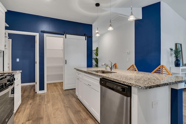 kitchen featuring sink, stainless steel appliances, a barn door, a center island with sink, and white cabinets