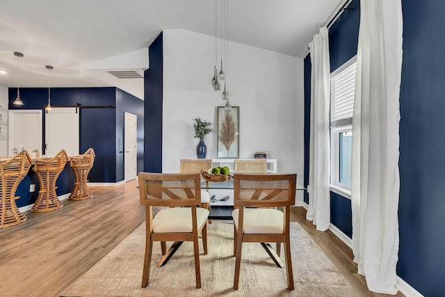 dining room featuring a barn door, lofted ceiling, and light wood-type flooring