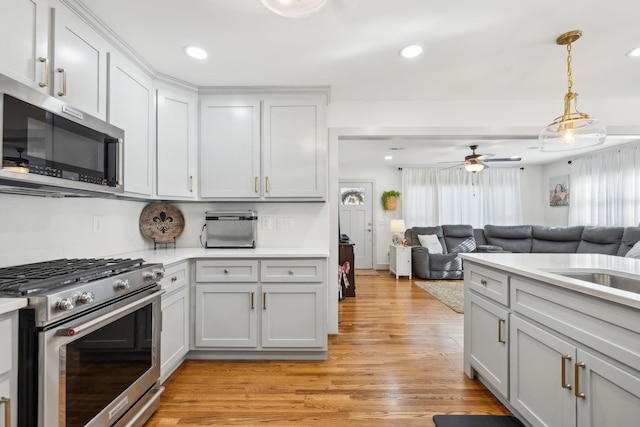 kitchen with ceiling fan, hanging light fixtures, stainless steel appliances, white cabinets, and light wood-type flooring