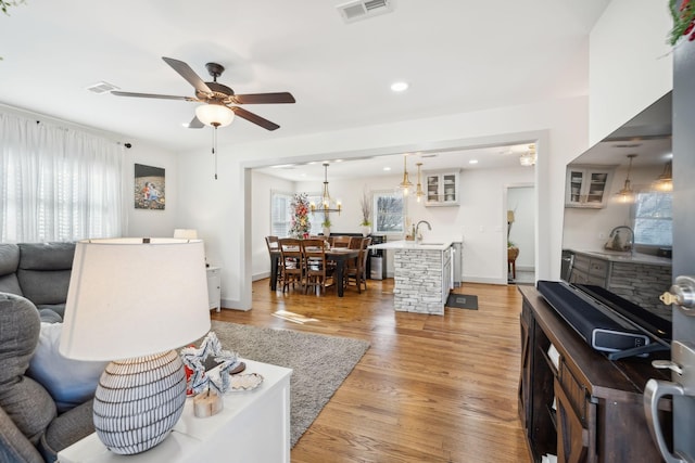 living room featuring ceiling fan with notable chandelier, light hardwood / wood-style floors, and sink