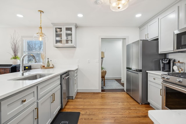 kitchen with hanging light fixtures, light wood-type flooring, sink, and appliances with stainless steel finishes