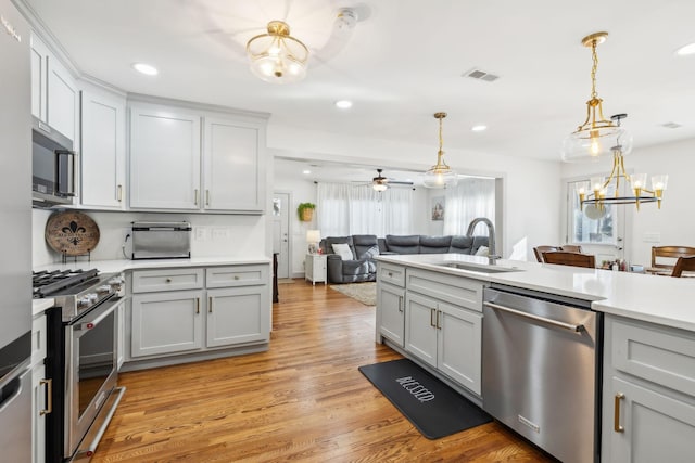 kitchen with pendant lighting, ceiling fan with notable chandelier, sink, light hardwood / wood-style flooring, and stainless steel appliances