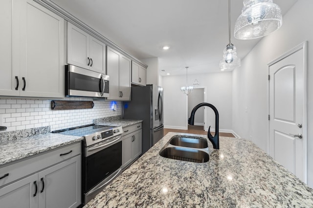 kitchen with gray cabinetry, light stone countertops, sink, decorative light fixtures, and appliances with stainless steel finishes