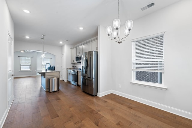 kitchen featuring a breakfast bar, a center island with sink, hanging light fixtures, dark hardwood / wood-style floors, and stainless steel appliances