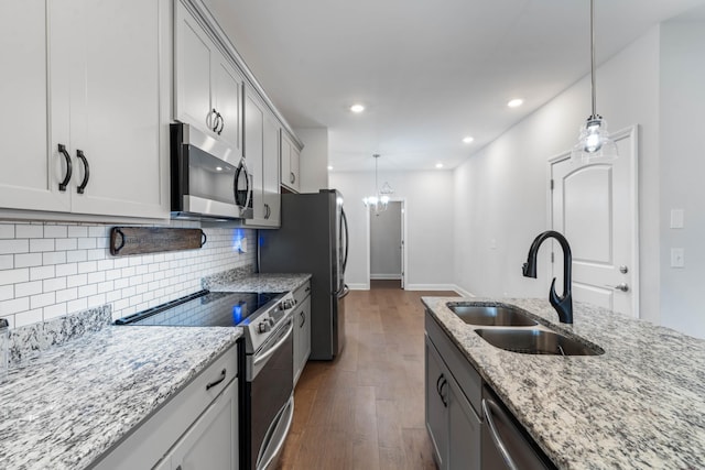 kitchen with light stone countertops, stainless steel appliances, dark wood-type flooring, sink, and a chandelier