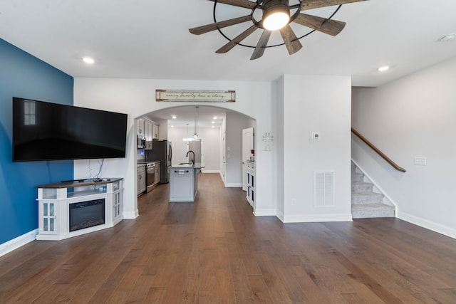 unfurnished living room featuring ceiling fan, sink, and dark wood-type flooring